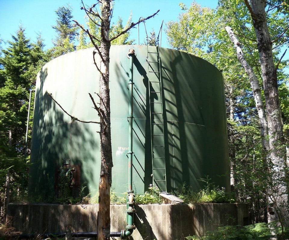 Réservoir cylindrique vert entouré d'arbres en milieu naturel, utilisé pour des études environnementales.