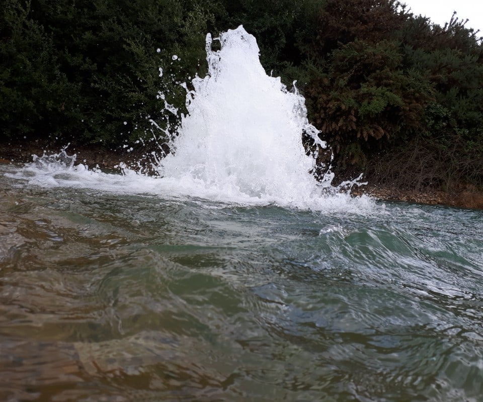 Éclaboussure d'eau à la surface d'un plan d'eau, entouré de verdure.